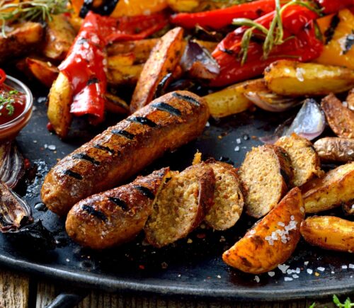 Grilled vegan soy sausages with hot sauce, potato wedges and vegetables