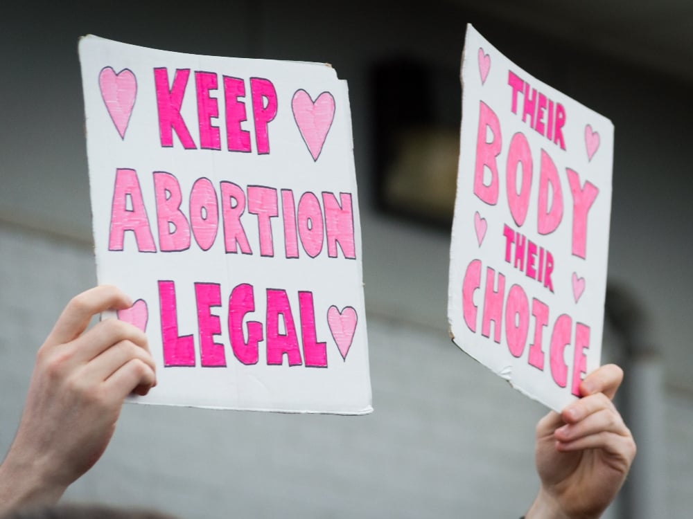 A person holds protest signs that say 'keep abortion legal' and 'their body their choice'