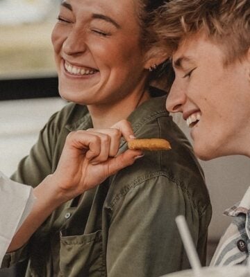 A person laughs while feeding another person plant-based nuggets