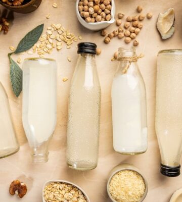 Six bottles of vegan milk lying down among nuts and seeds