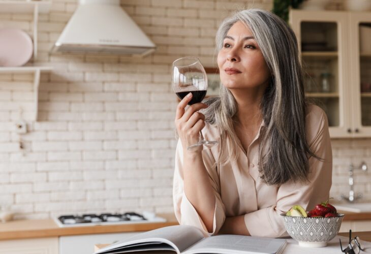 A woman reads in her kitchen drinking wine