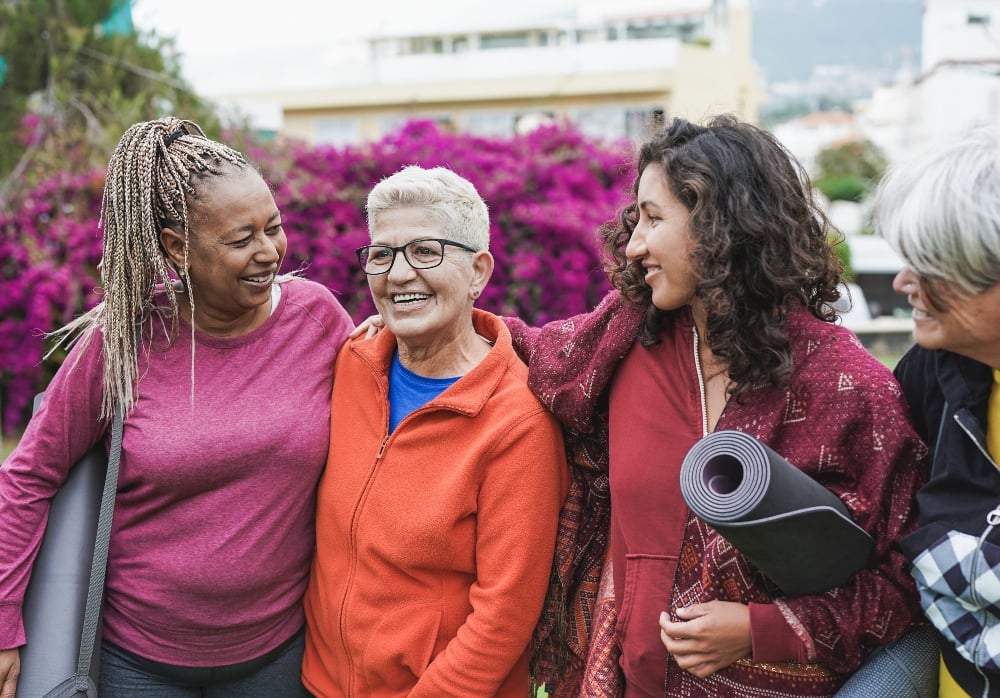 Four healthy older women outdoors holding yoga mats