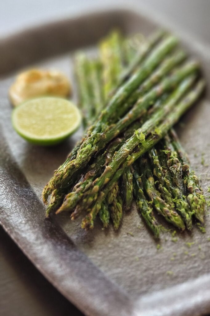 Grilled asparagus next to a portion of vegan lime miso mayo and cut fruit