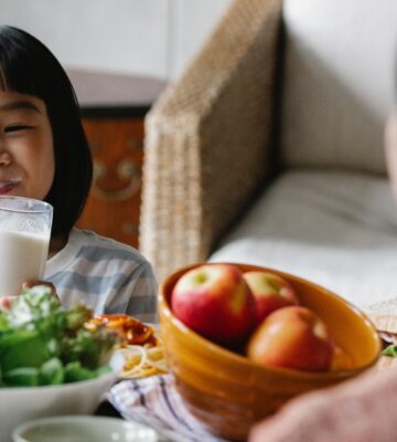 A child smiling and drinking milk with salad and fruit on the table