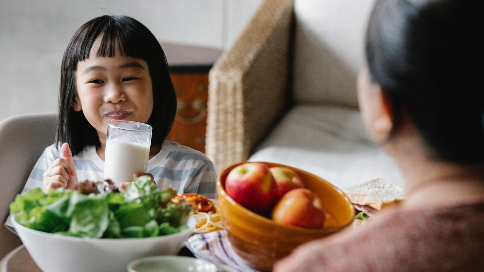 A child smiling and drinking milk with salad and fruit on the table