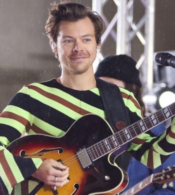 Harry Styles holds a guitar while on stage