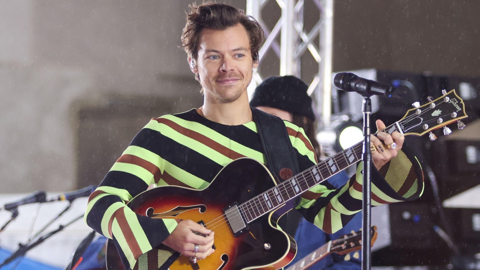 Harry Styles holds a guitar while on stage