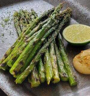Grilled asparagus next to a portion of vegan lime miso mayo and a cut lime