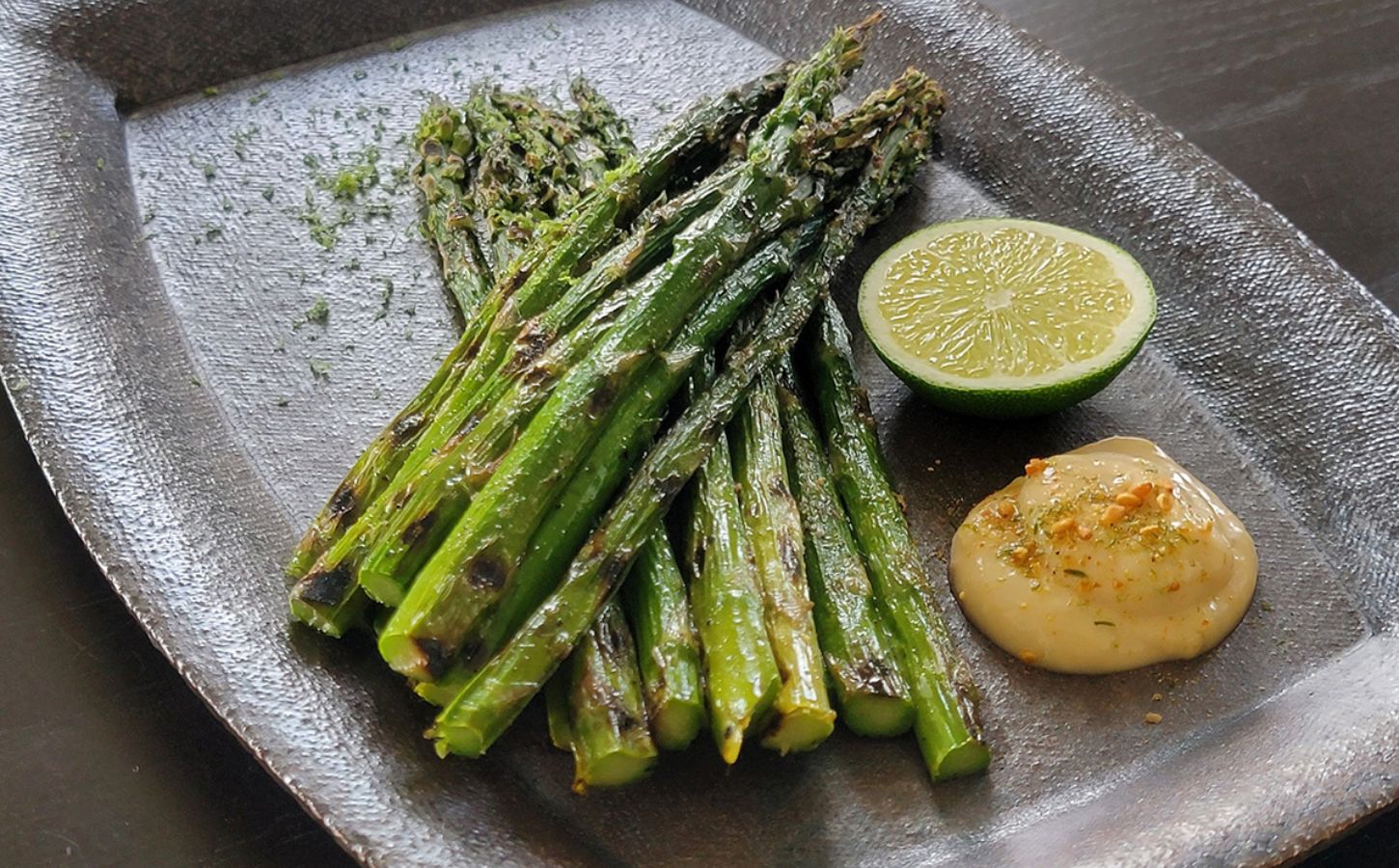 Grilled asparagus next to a portion of vegan lime miso mayo and a cut lime