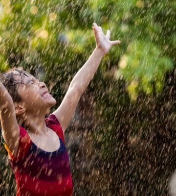 a child with their arms out in the rain
