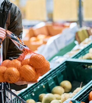 woman buying oranges in plastic mesh at supermarket