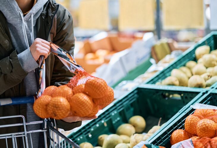 woman buying oranges in plastic mesh at supermarket