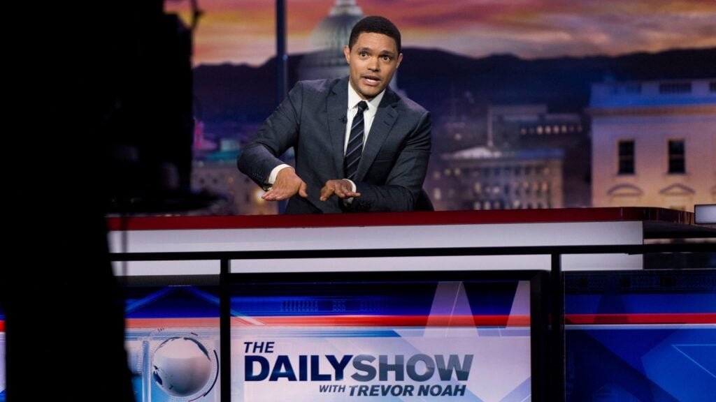 Trevor Noah sits on his desk at the Daily Show