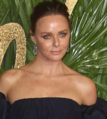 Stella McCartney poses on a red carpet with a green background