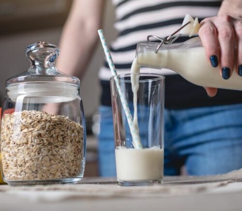 A person pouring oat milk into a glass
