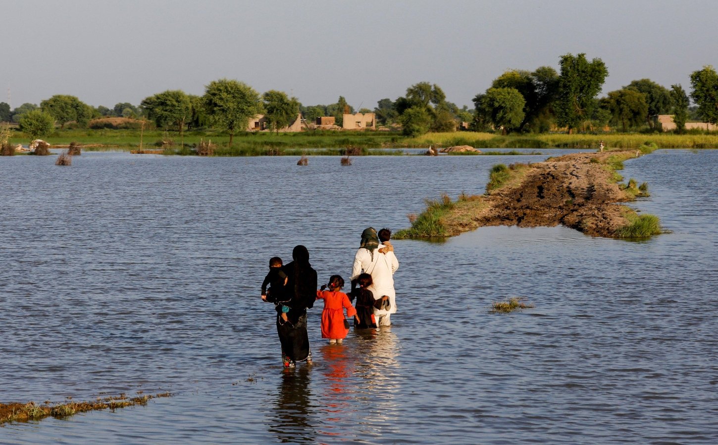 A family walks amid flood waters on their way to their village in Mehar, Pakistan