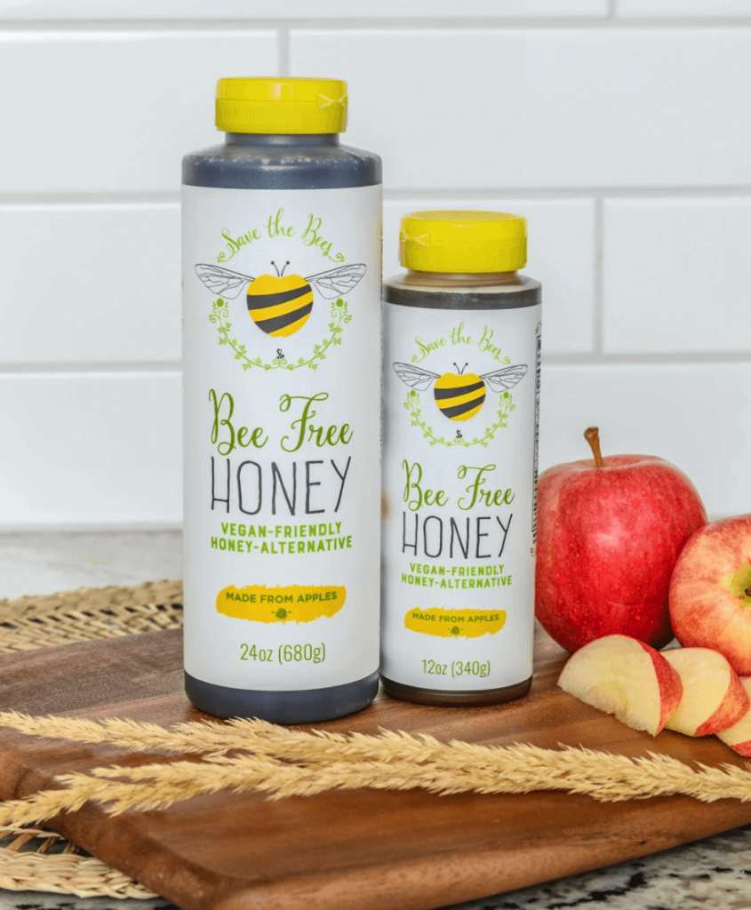 Two bottles of vegan honey made by Bee Free on a kitchen counter next to some apples