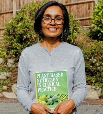 Dr Kassam holding up the a plant-based text book in a garden