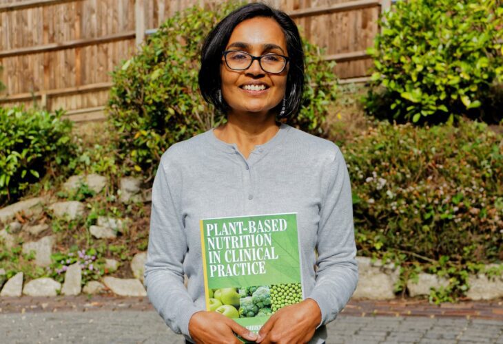 Dr Kassam holding up the a plant-based text book in a garden