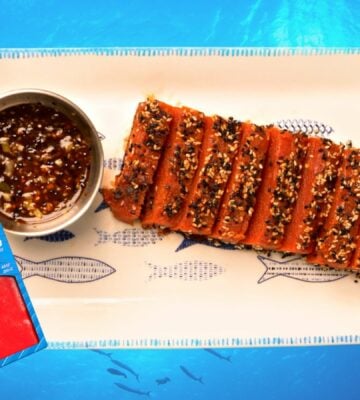 Grilled vegan tuna steak on a plate beside a box of Current Foods tuna, with an ocean blue background