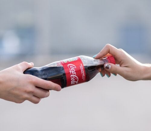 Two people hold a coca-cola plastic bottle