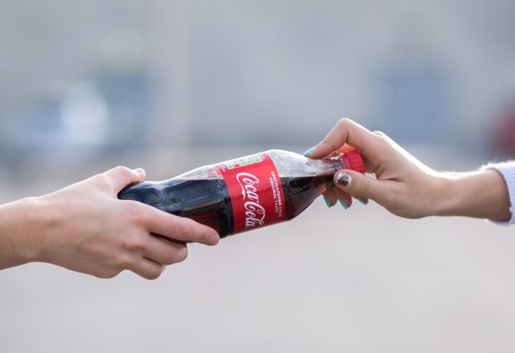 Two people hold a coca-cola plastic bottle