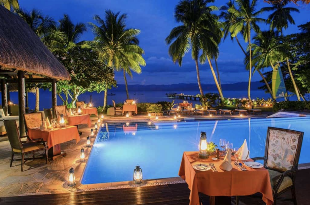 An outdoor dining area by a swimming pool surrounded by palm trees