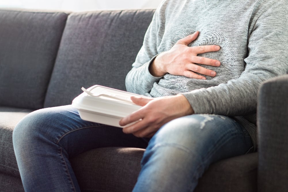 A man holds his stomach and an empty food takeaway container