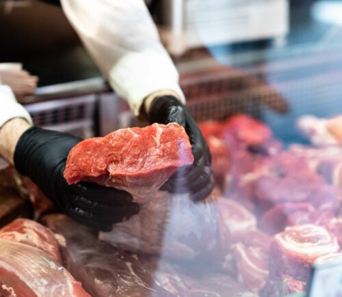 a butcher holds a slab of meat at the meat counter