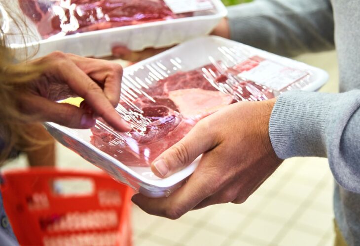 A person holds beef meat in a white plastic tray in a supermarket