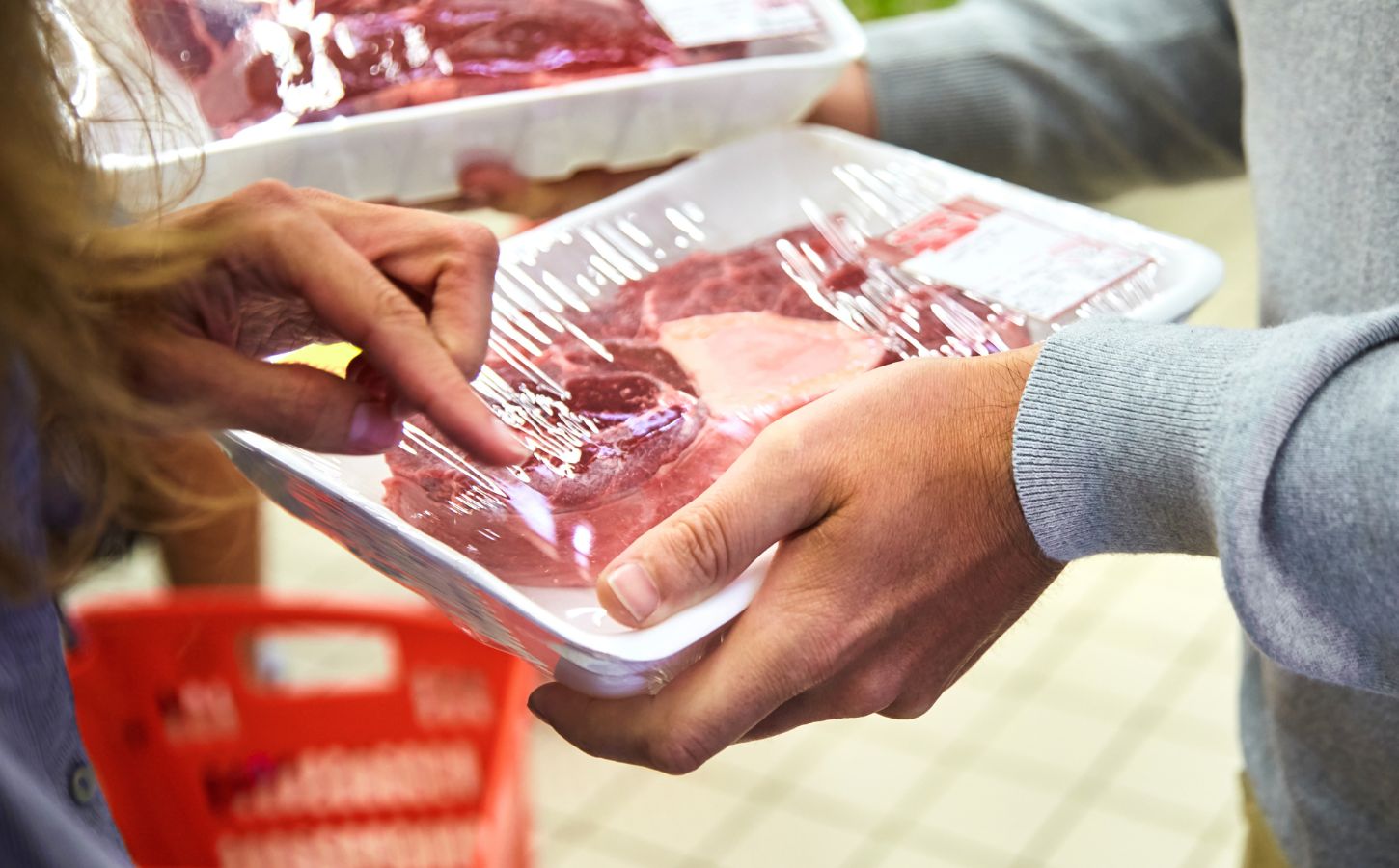 A person holds beef meat in a white plastic tray in a supermarket