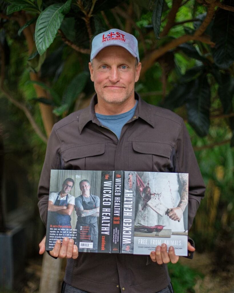Vegan actor Woody Harrelson holding Wicked Kitchen's plant-based recipe book