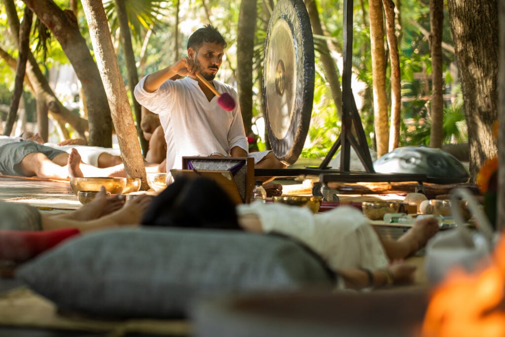 A man playing the gong as resort guests meditate around him