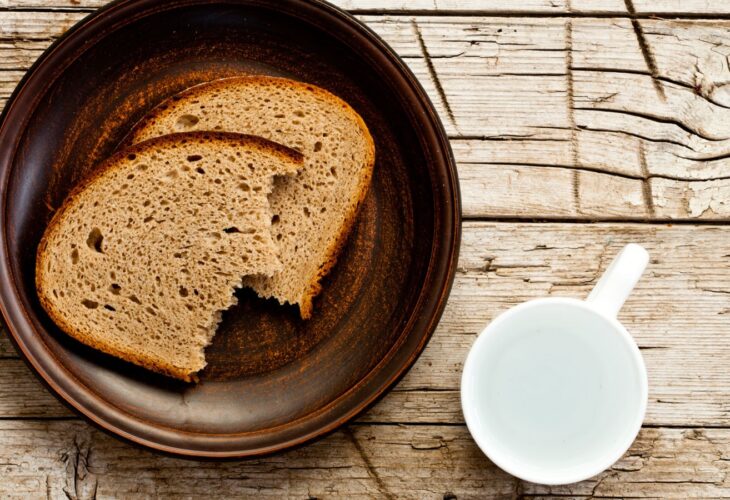 Two pieces of bread on a brown plate beside a white cup