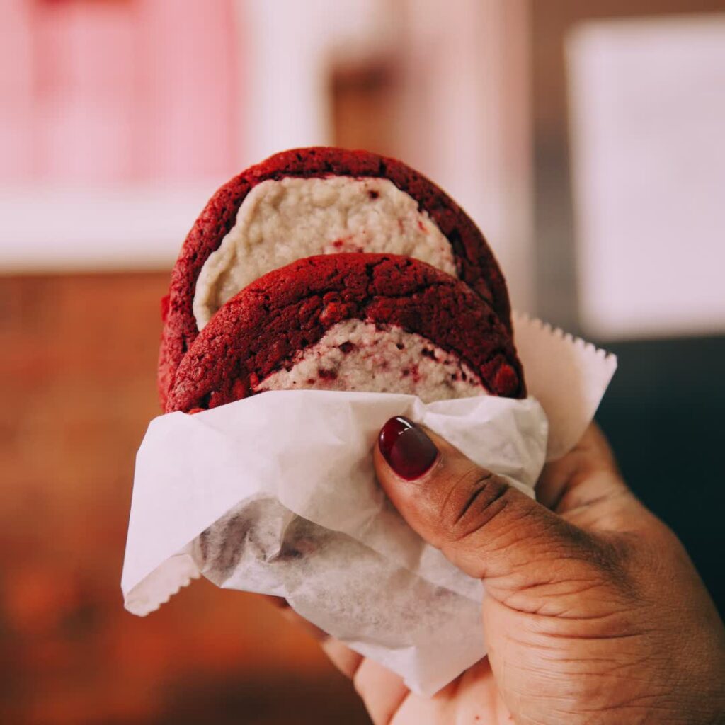 A hand holding a vegan red velvet cookie by Sofia & Grace