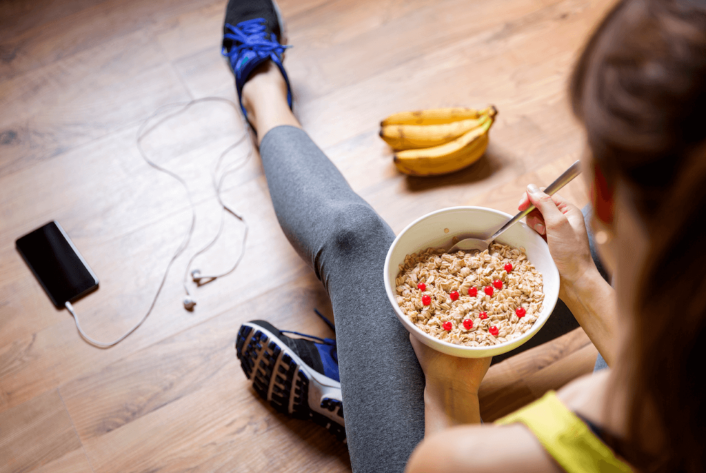 Woman eating oatmeal with berries wearing fitness gear and sitting on the floor