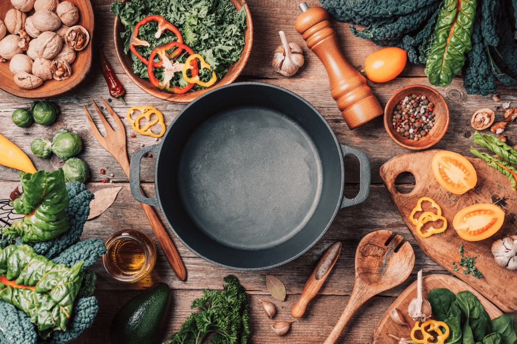 Organic vegetables, an empty cooking pot, wooden bowls, and spoons on a wooden background