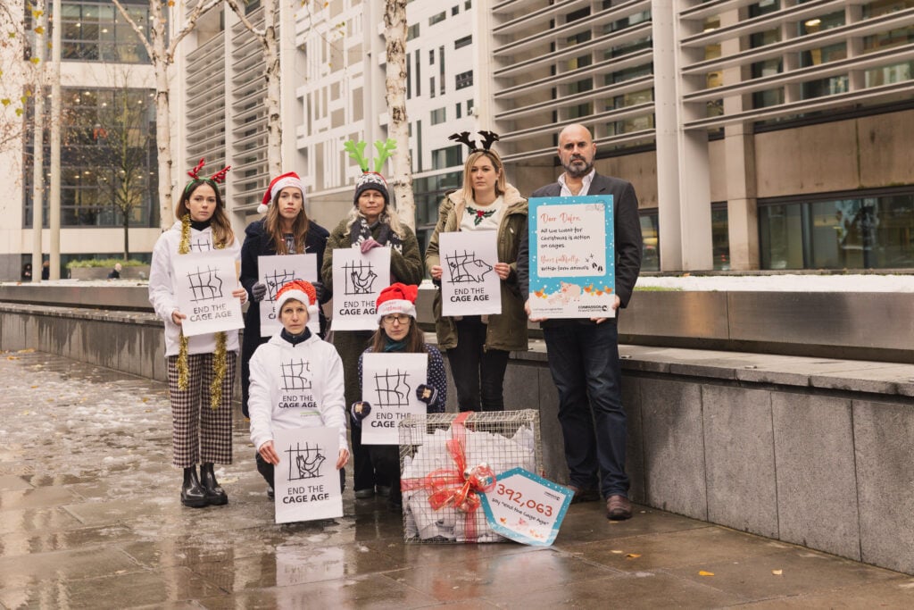 Campaigners holding signs urging the government to ban cages for farmed animals