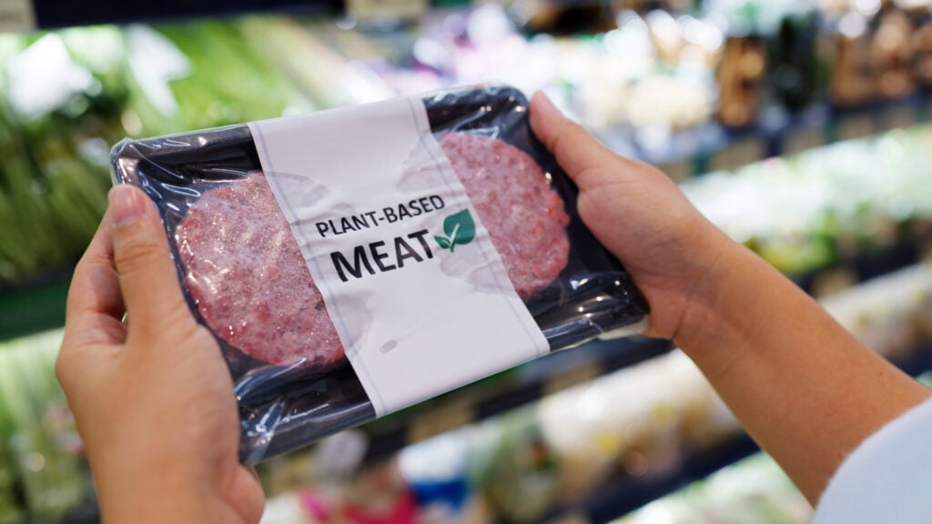 A person picking up a pack of vegan meat off the supermarket shelves