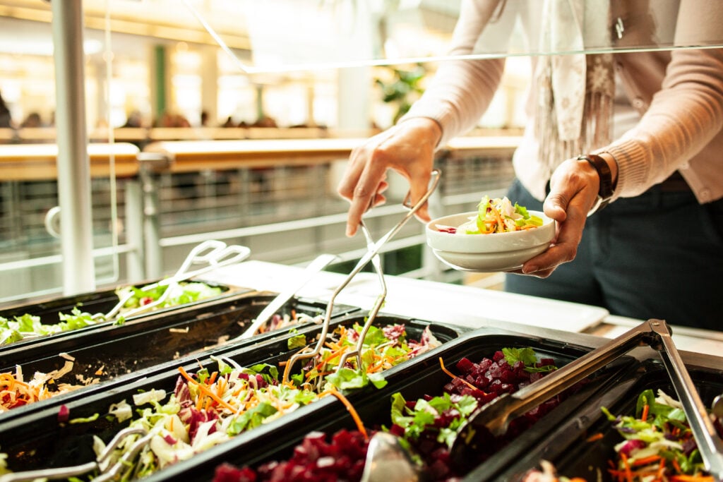 A woman serving herself plant-based food in a cafeteria