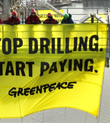 Greenpeace activists holding a banner reading "stop drilling, start paying" while occupying a Shell oil platform