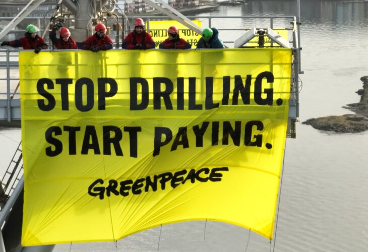 Greenpeace activists holding a banner reading "stop drilling, start paying" while occupying a Shell oil platform