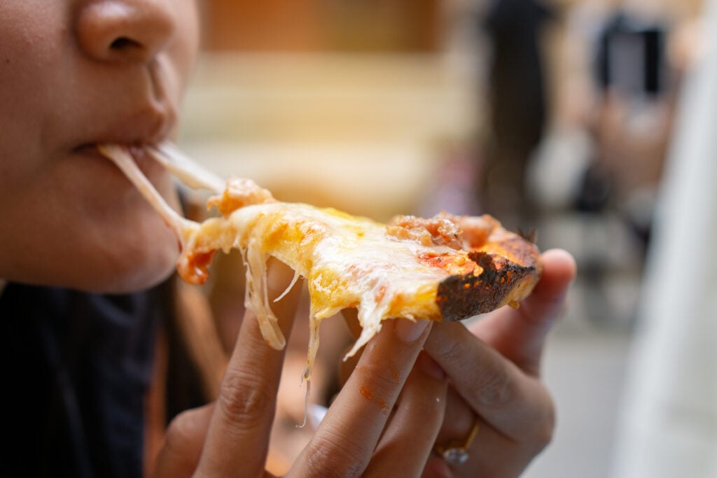 A person eating a slice of pizza with dairy cheese