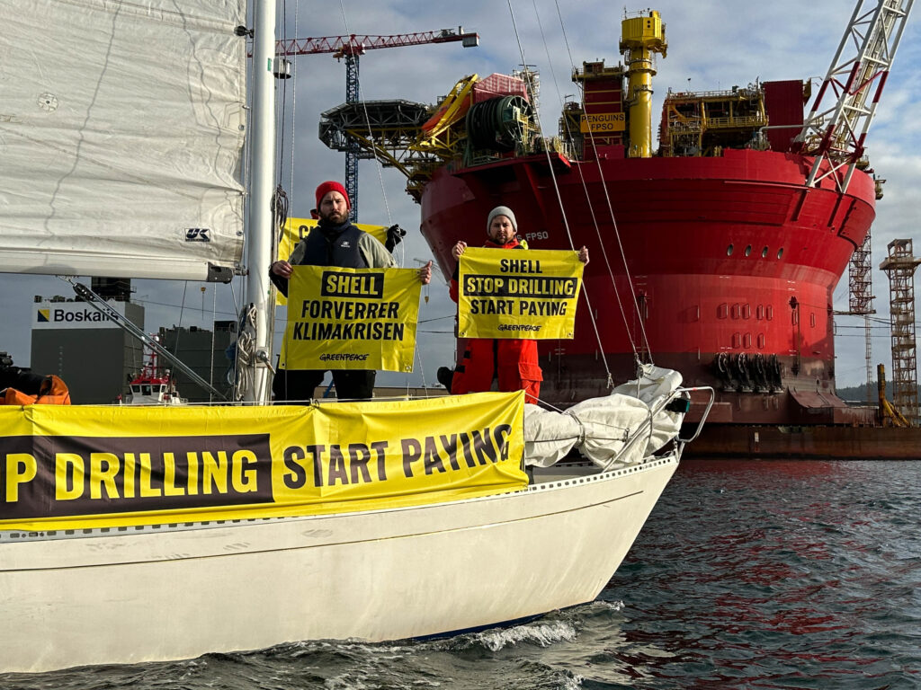 Greenpeace activists holding a banner reading "stop drilling, start paying" while occupying a Shell oil platform