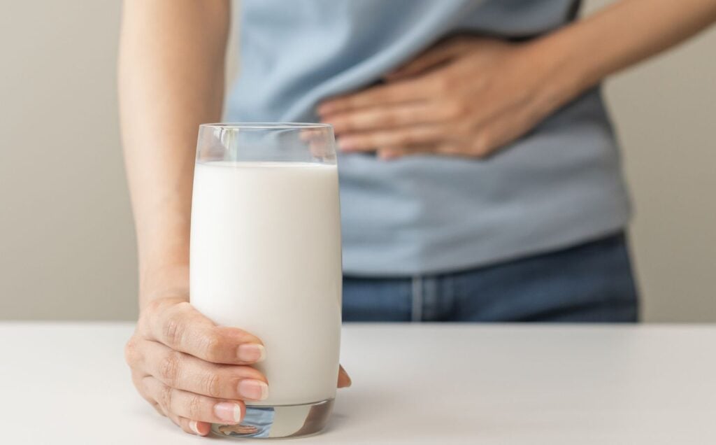 A person holding their stomach and a glass of dairy milk
