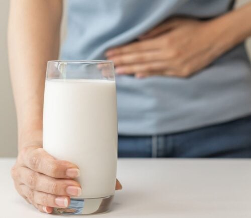 A person holding their stomach and a glass of dairy milk