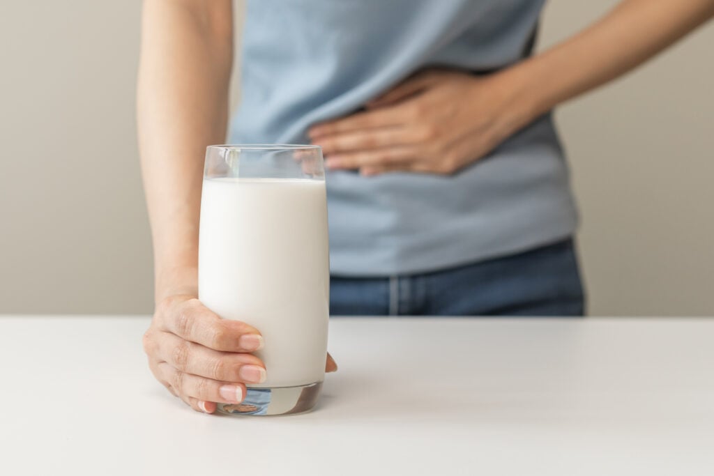 A person holding their stomach with one hand a glass of dairy milk with the other