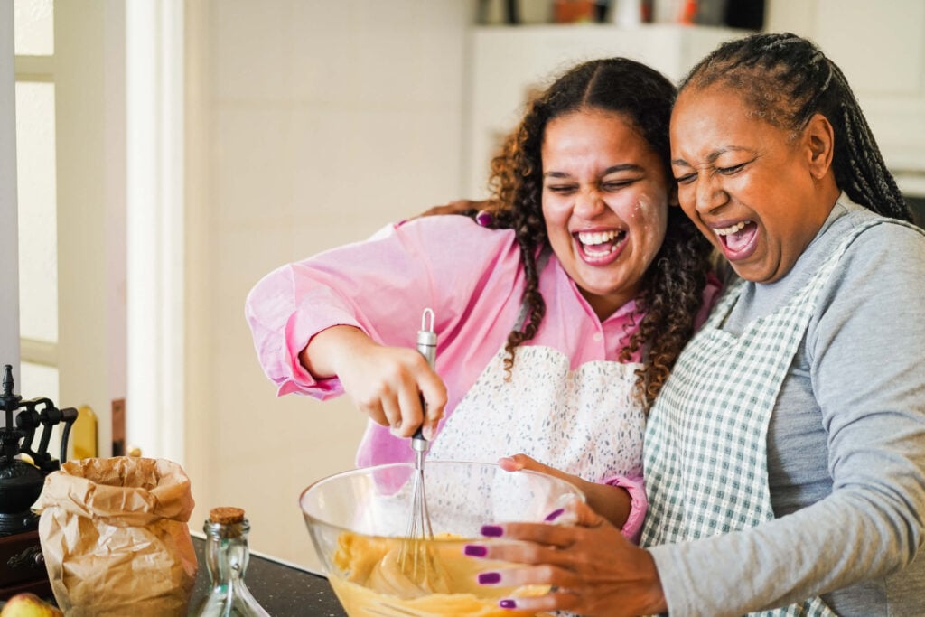 A laughing mother and daughter prepare plant-based food in the kitchen together