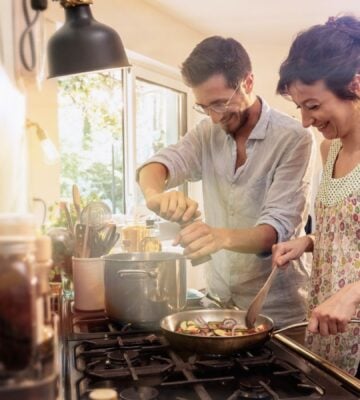 A couple cooking vegan meals in a kitchen using various cookware and appliances