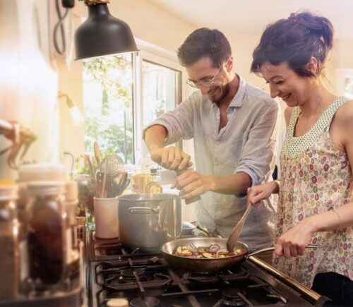 A couple cooking vegan meals in a kitchen using various cookware and appliances
